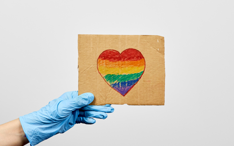 LGBTQ friendly healthcare system worker holding handmade placard with heart-shaped rainbow flag